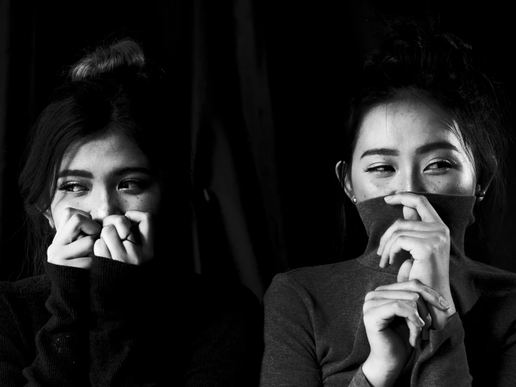 two young women sitting down and posing for the camera