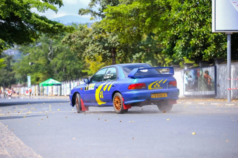 blue racing car with yellow and red stripes drives through the road