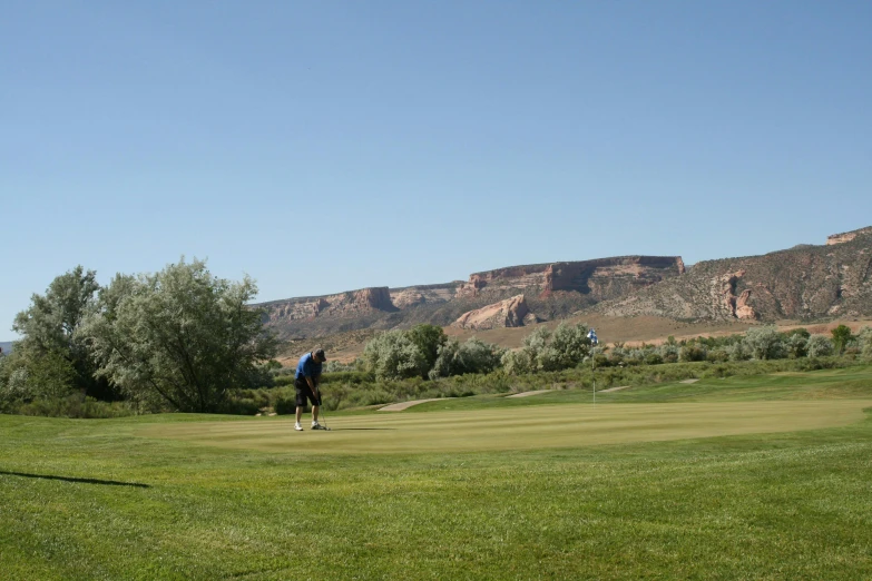 a man standing on a golf green with a mountains range in the background