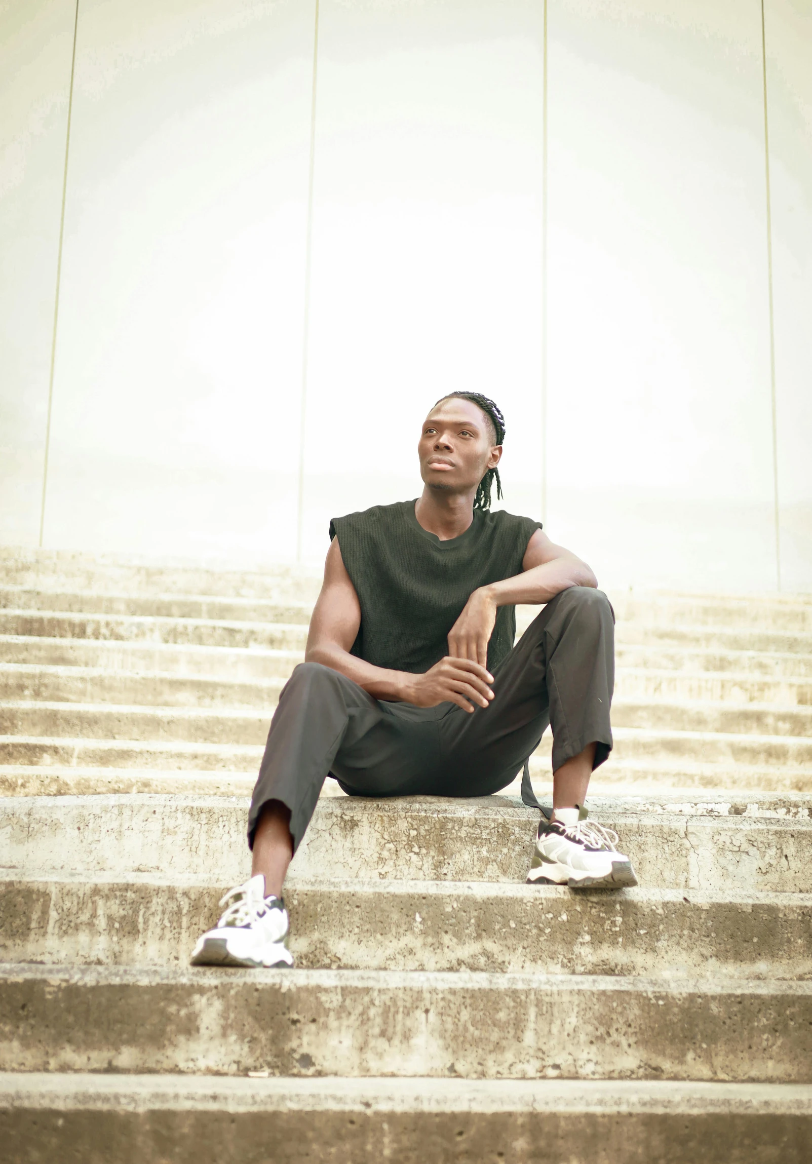 man sitting on stairs, wearing white sneakers and looking up