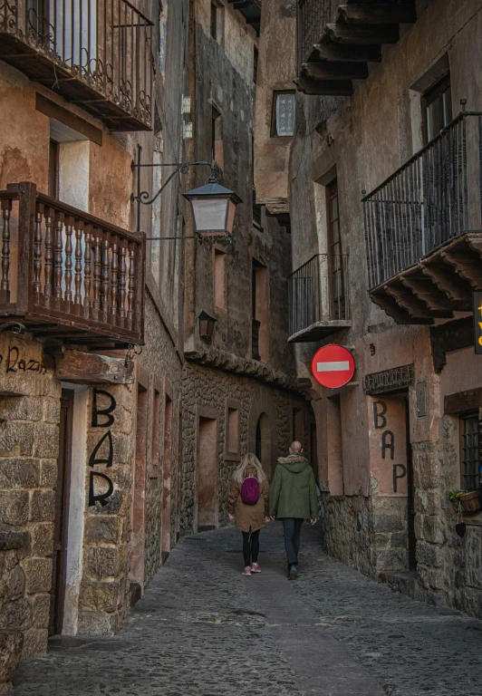 two people walking down an alley way on either side of a traffic sign