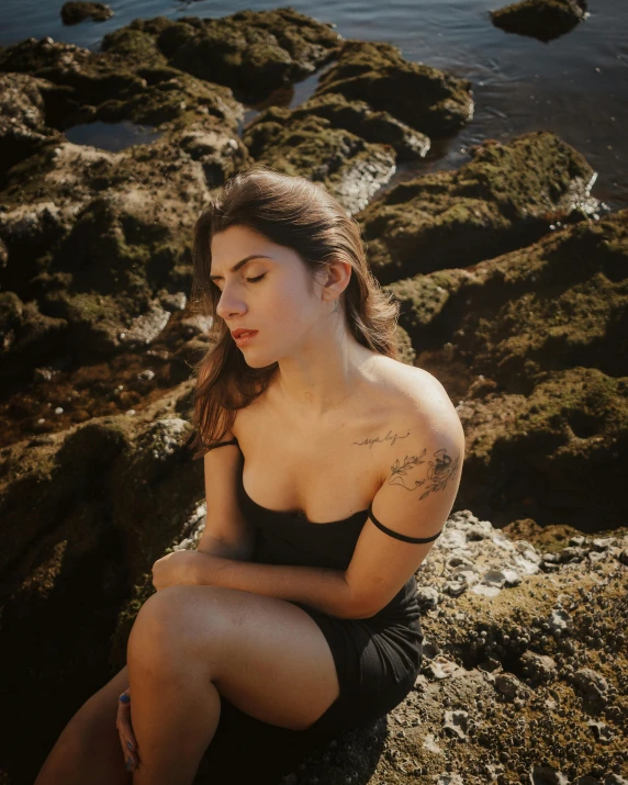 a girl sitting on top of a rocky shoreline near the water