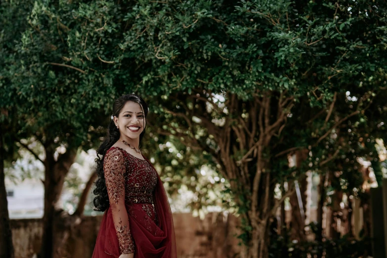 a woman in a red dress smiling and standing under some trees