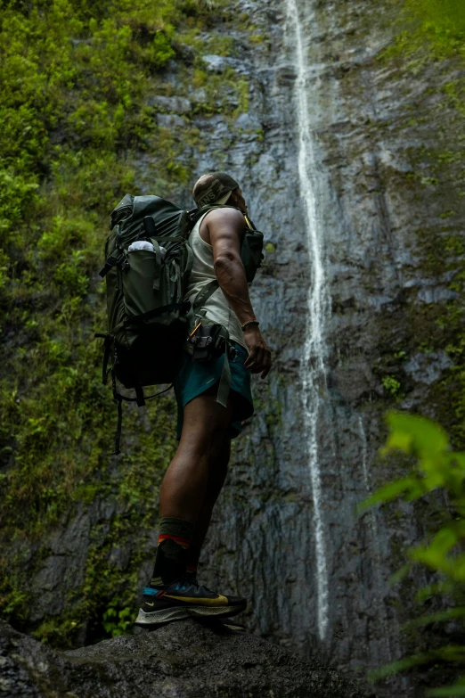 a man with a backpack standing in front of a waterfall