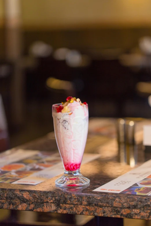 a small milkshake with strawberries sits on a wooden counter top