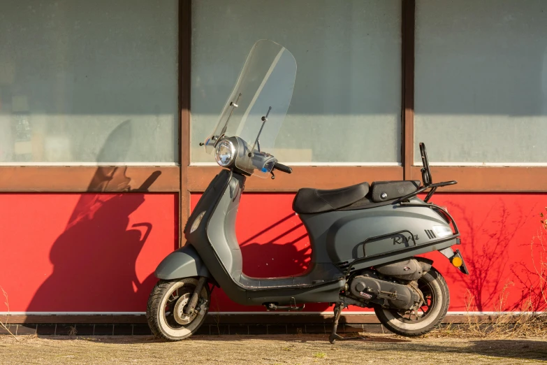 a scooter parked against a red building next to a tree