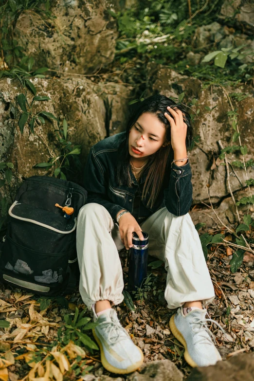 young asian woman with backpack sitting on ground and holding coffee