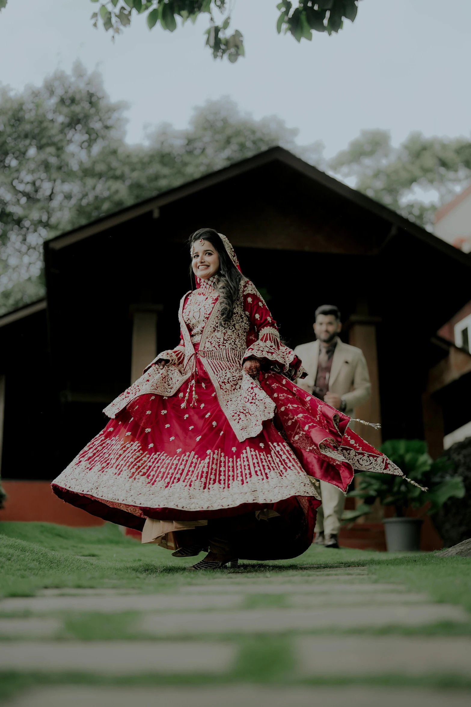 an indian couple dressed in red pose outside a house