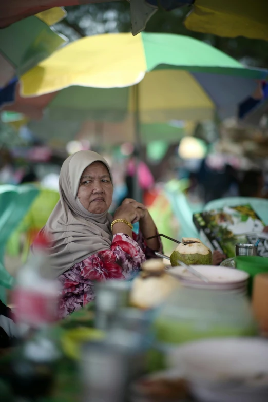 an older woman sitting under an umbrella at a picnic