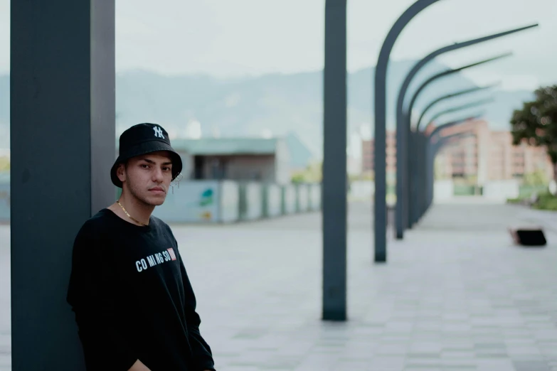 man in black shirt leaning against post with buildings on background