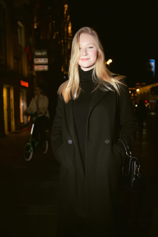 a woman in a black coat is standing on a dark street