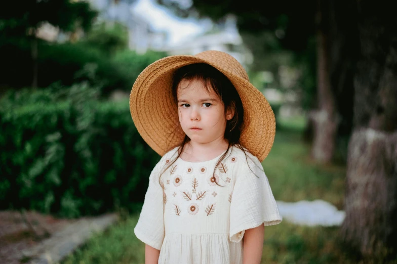 a little girl standing outside wearing a large brown hat