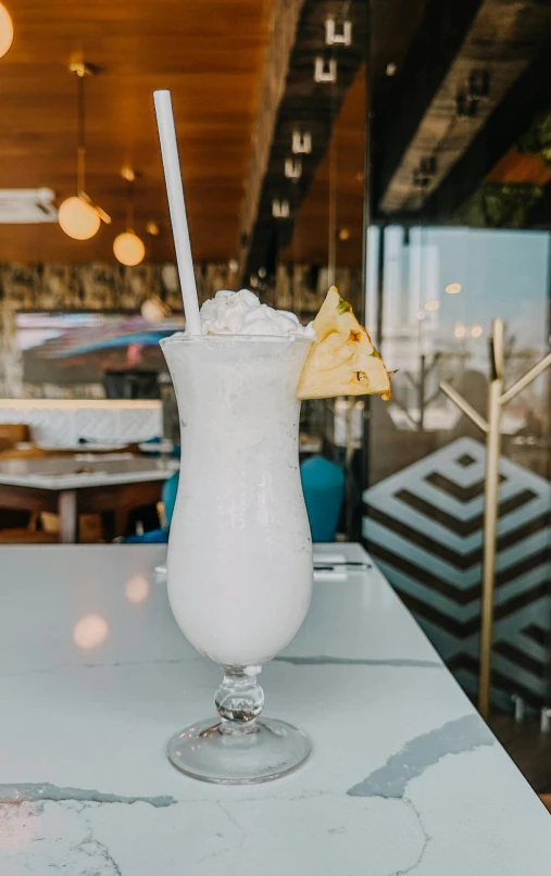 a white drink with a slice of pineapple on the rim