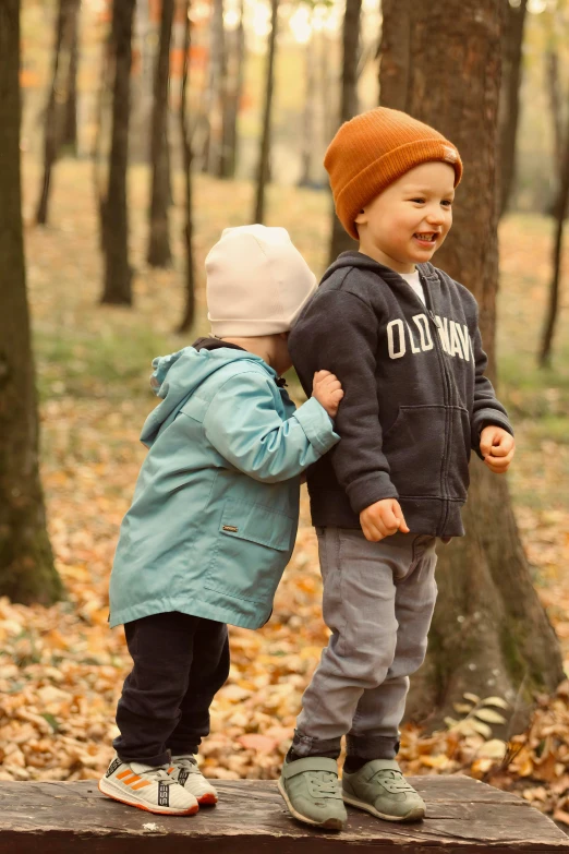 two young children in jackets playing together in the woods