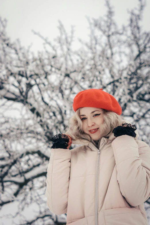 a woman wearing a pink jacket, a red hat and holding her hands to her hair