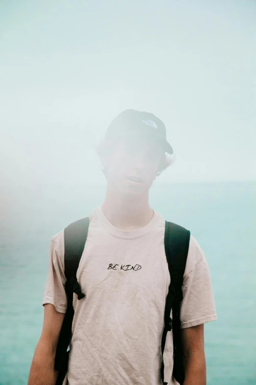 young man standing next to the ocean with sun shining on him