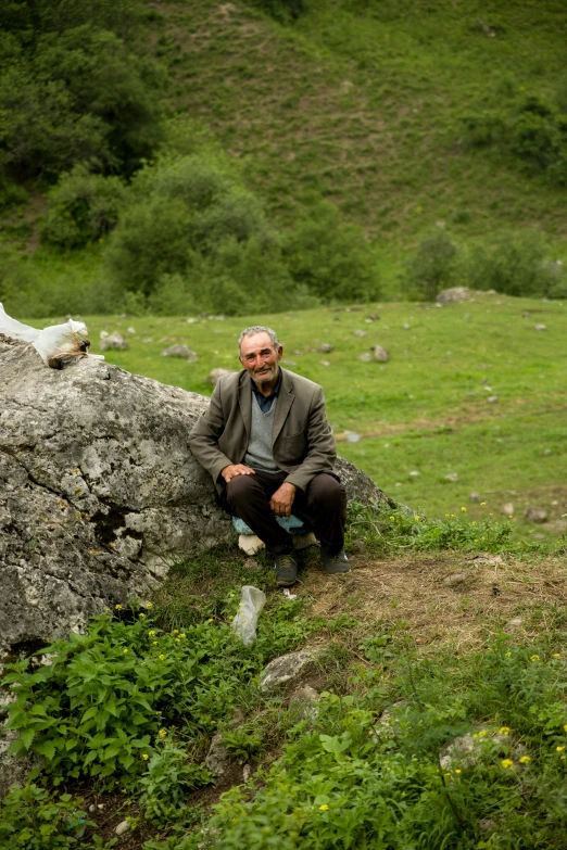 a man sits on a rock near a field and mountains