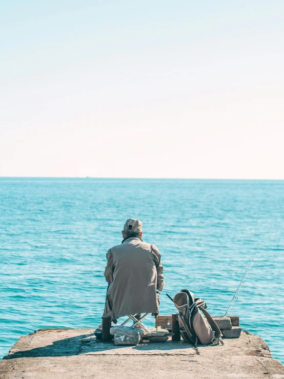 man sitting on pier with backpack fishing from lake