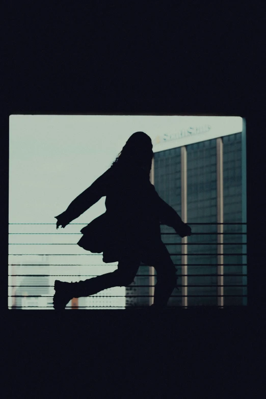 a silhouette of a girl holding her arms out in the air, with the wall in the background