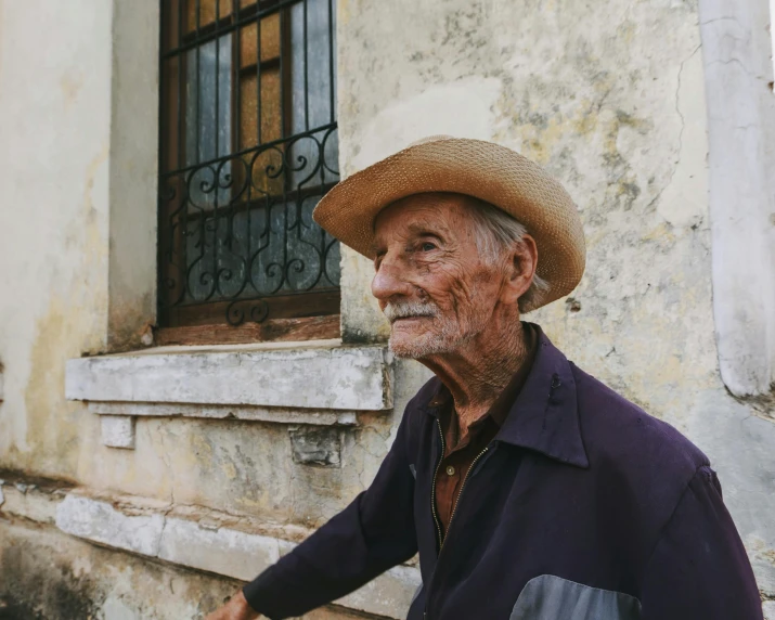 old man with hat sitting on ledge near window