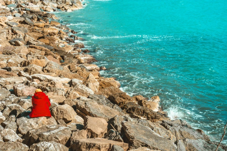 a person in a long red gown standing on rocks by the water