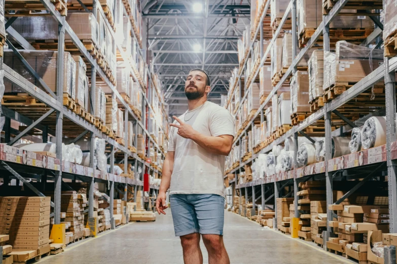 a man walks down a large warehouse floor using his phone