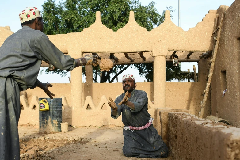 two people playing with objects outside a mud hut