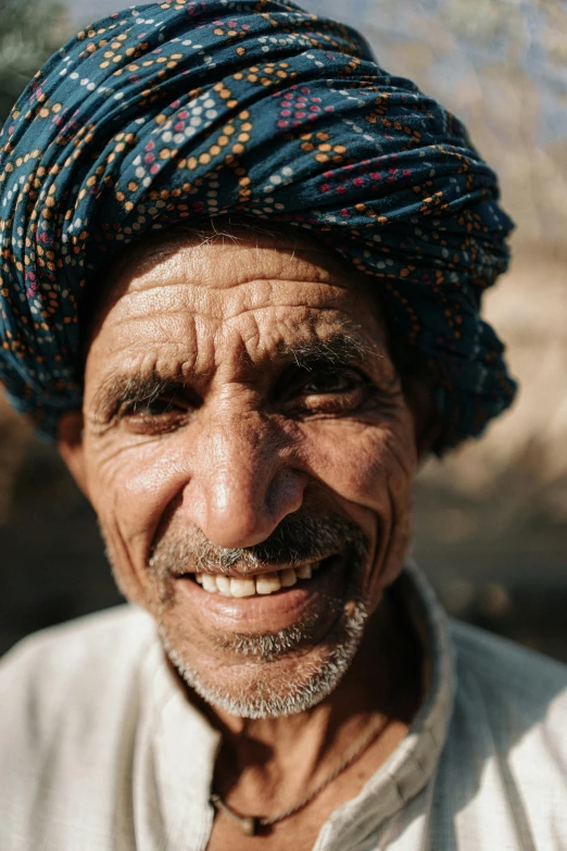 an older man wearing a blue turban standing next to trees