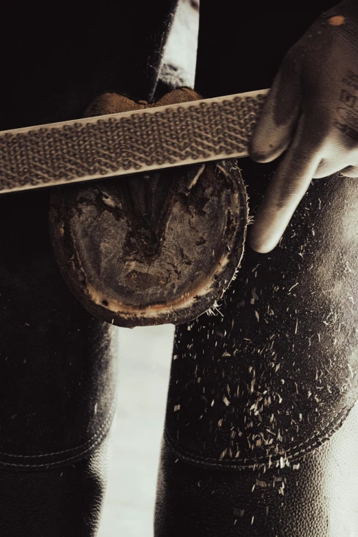 a hand that is holding a piece of wood in front of a pair of boots