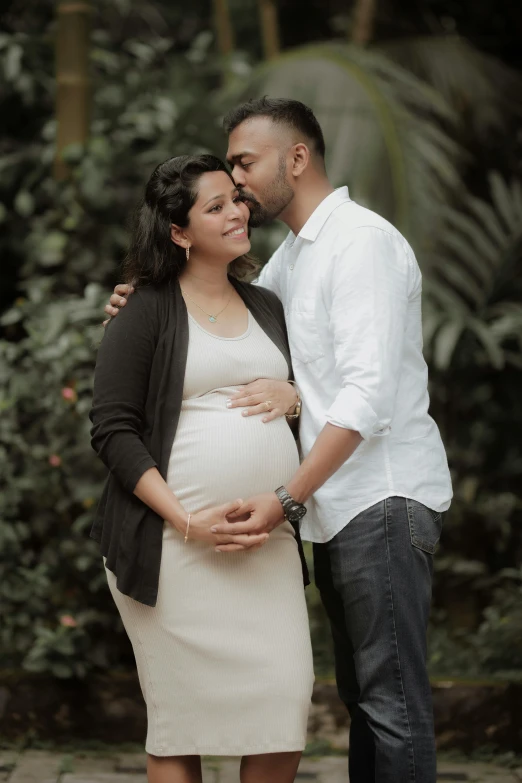the pregnant couple stands next to each other smiling at each other