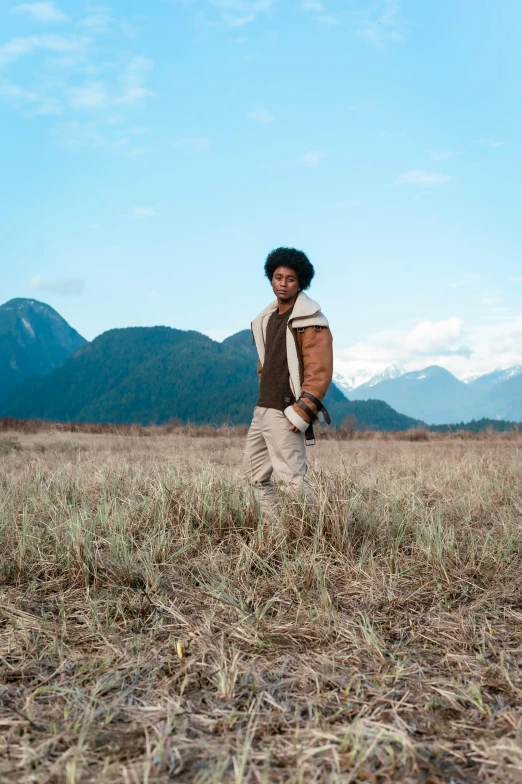 a man standing in the middle of a field with mountains in the distance