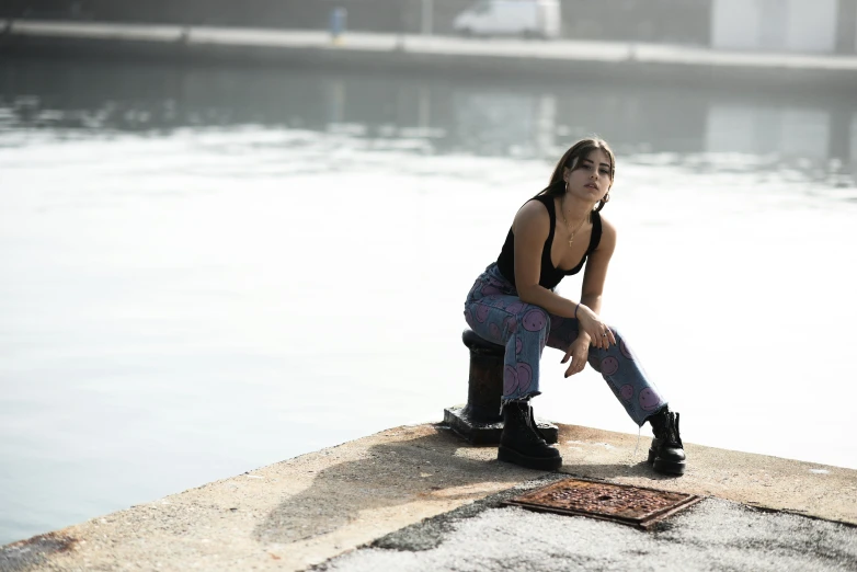 a woman in black and purple pants sitting on top of a ledge next to the water