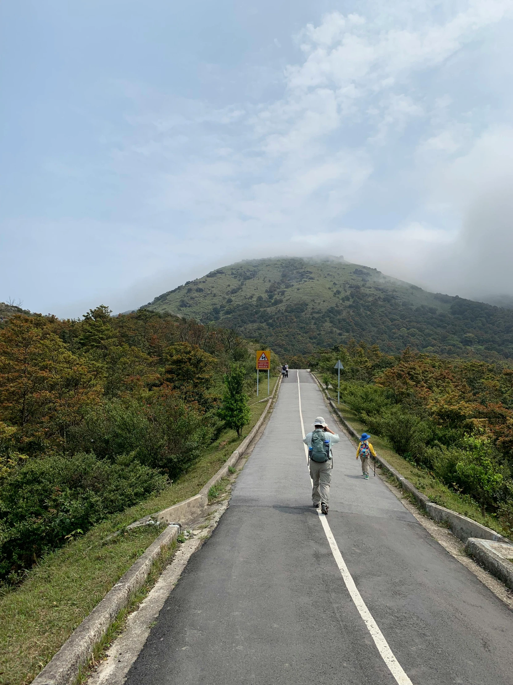 people riding bikes on an empty road near a hill