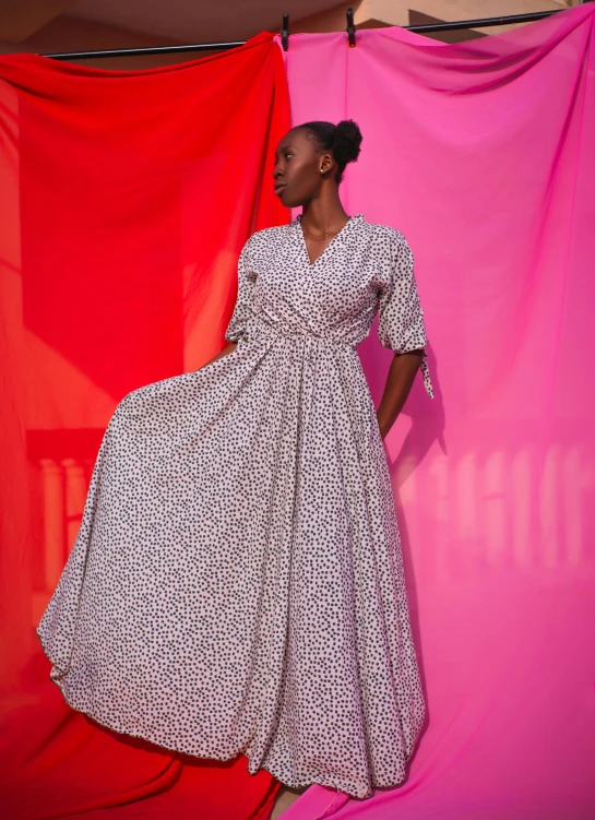 a young woman in a long dress is standing beside a pink backdrop