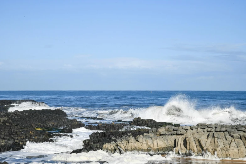 waves crashing over a rocky shoreline under a blue sky