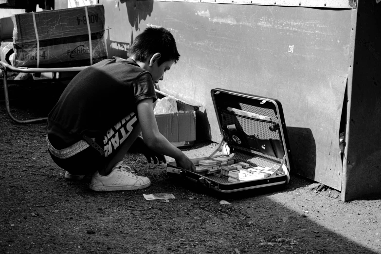 black and white image of boy kneeling next to opened briefcase