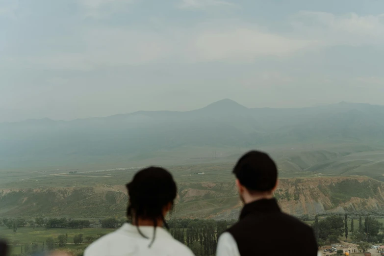 two people standing on a hilltop overlooking a valley with a cloudy sky