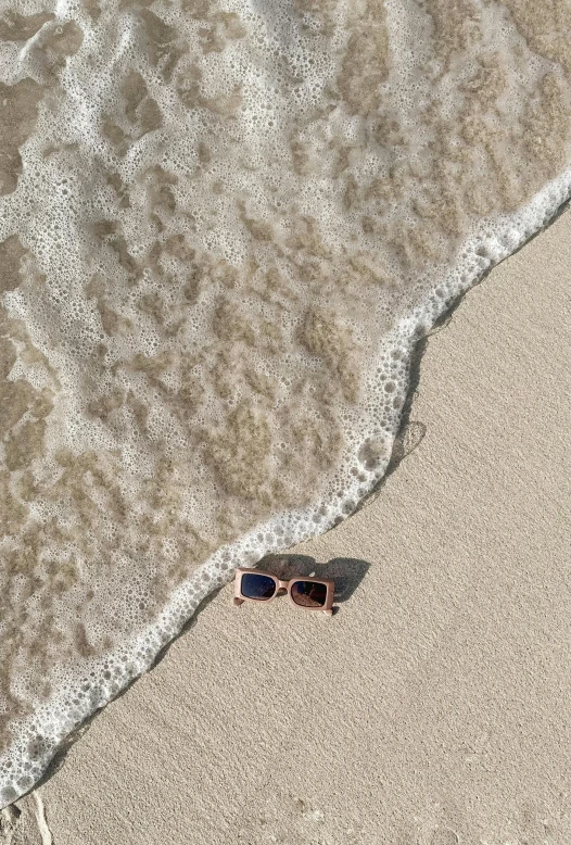 some sort of pair of sunglasses sitting on the sand by the water