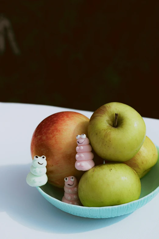 an apple and toy worms in a bowl