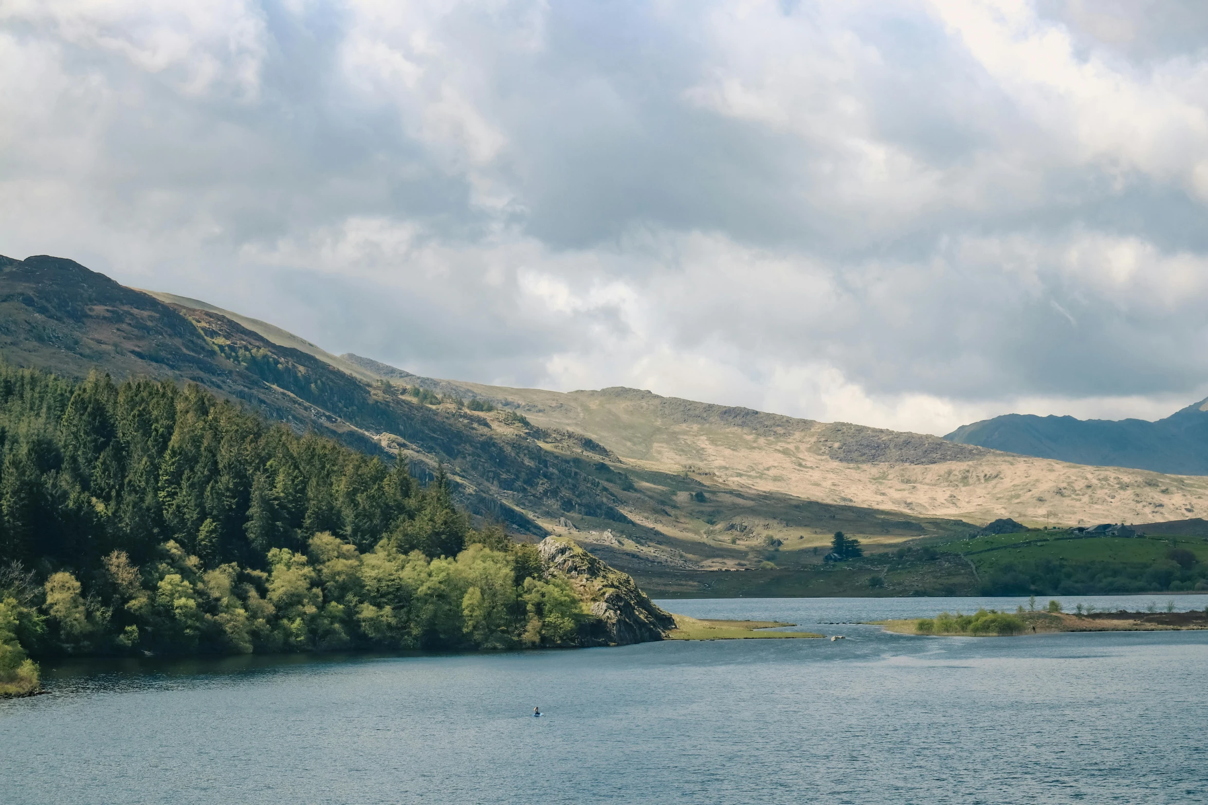 a lake surrounded by lush green mountains under cloudy skies