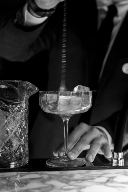 someone pouring a drink into a coupe glass