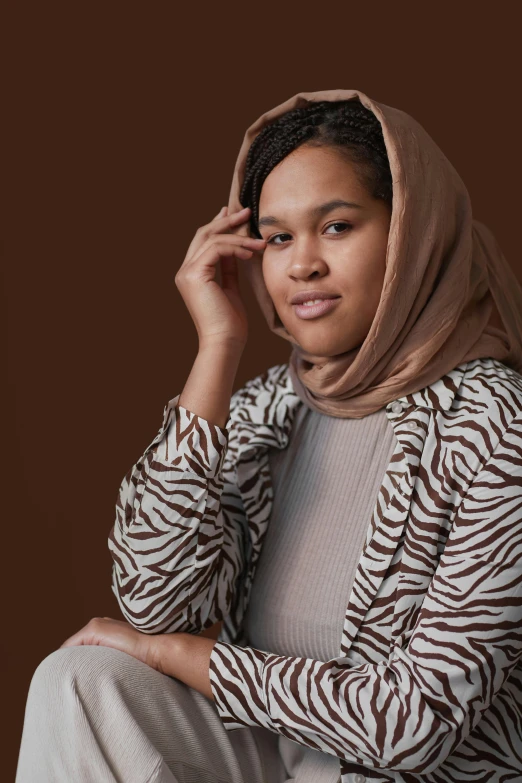 a woman wearing a brown head scarf sits on a stool