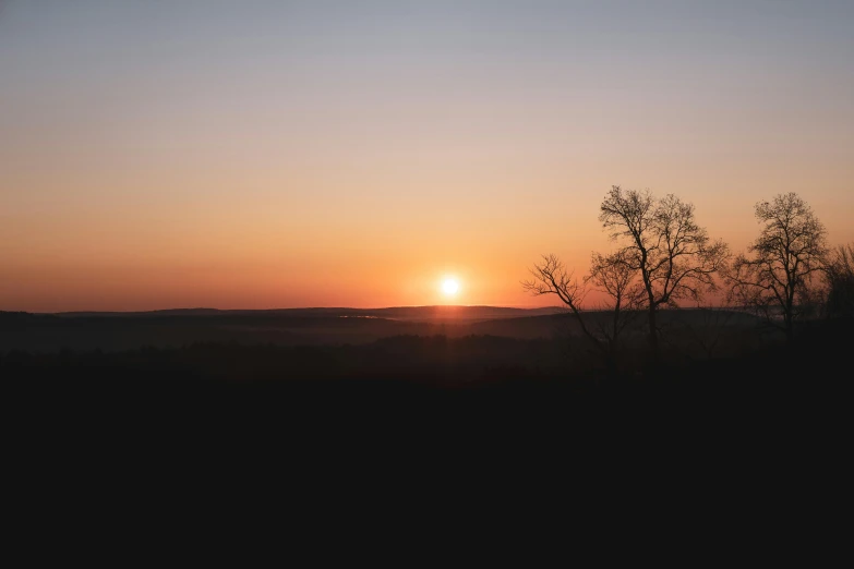 the sun is setting behind the silhouettes of trees