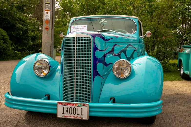 a classic turquoise car parked in front of a green tree