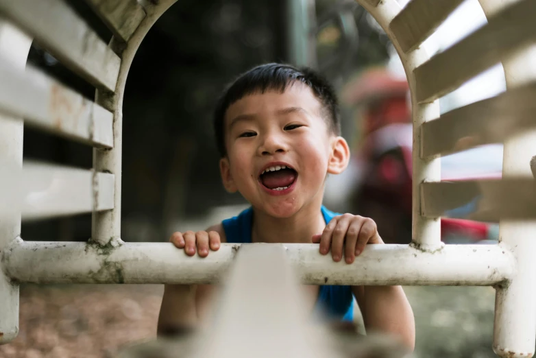 a little boy looks through the bars of a children's wooden train track