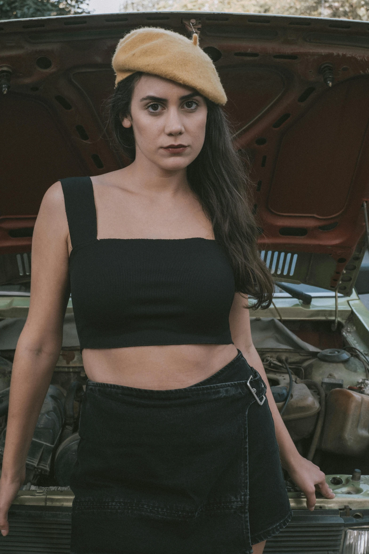 a young woman in a black skirt and crop top standing next to a car