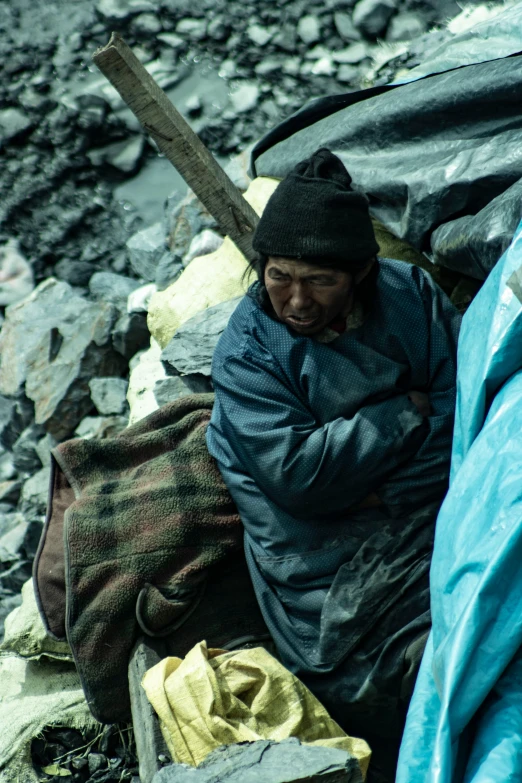 a man sitting on rocks, sleeping in a sleeping bag