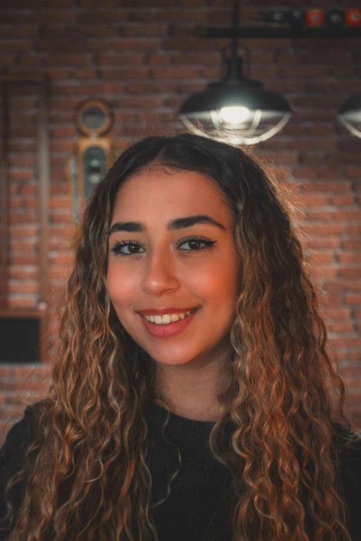 a woman with long, curly, brown hair is smiling in a cafe