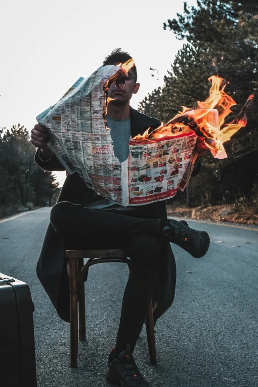 a man sits on a chair next to a burning piece of luggage