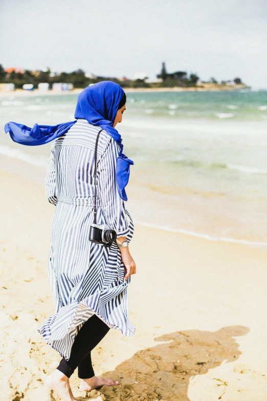 a woman walking on a beach carrying a blue bag